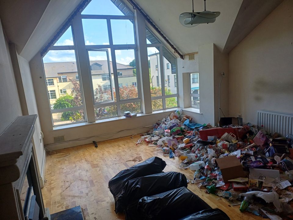 Apartment living room with a vaulted window, full of bags and belongings before clearance